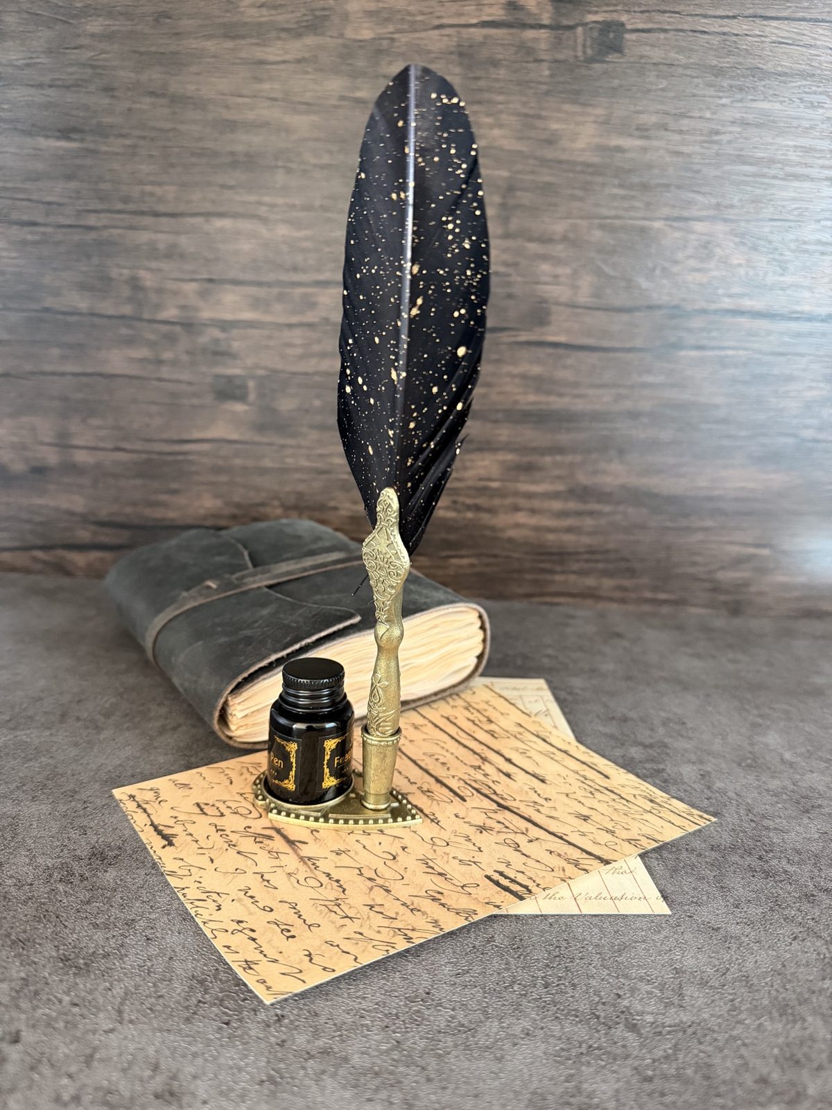 Black feather pen, ink, leather journal, and handwritten papers